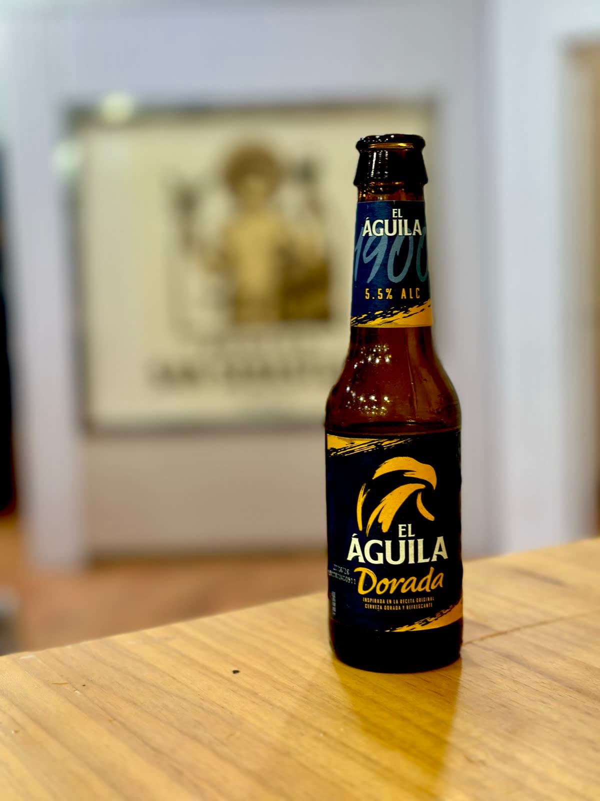 Botellín de El Águila Dorada sobre la barra, con el santo de la casa al fondo